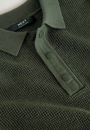 Grünes gestricktes Poloshirt mit strukturiertem Muster, Kragen und drei dunkelgrünen Knöpfen. Pflegeetikett zeigt 'NEXT, hergestellt in Myanmar.'