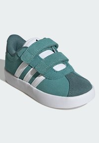 Tyrkysové nubukové tenisky s bílými pruhovanými detaily a suchými zipy. Zaoblená špička a texturovaná tkanina na jazyku a patě. Gumová podrážka.