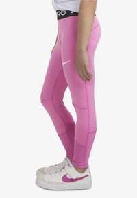Leggings fucsia aderenti con una alta vita nera caratterizzata da un logo bianco, pannelli testurizzati e cuciture a contrasto. Indossati con sneaker bianche.