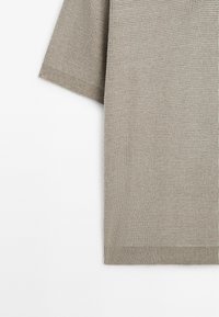 Top in maglia beige texturizzato con maniche corte, vestibilità rilassata e orlo a costine. Il tessuto ha un aspetto intrecciato e morbido.