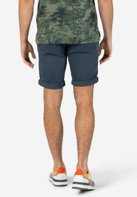 Navy rolled-cuff shorts made of lightweight fabric, with a smooth texture. Worn with multicolored sneakers featuring orange accents.