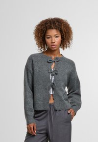 Grauer gestrickter Cardigan mit verkürztem Saum, runder Ausschnitt und drei dekorativen Bändern an der Vorderseite. Lange Ärmel und weicher Griff.