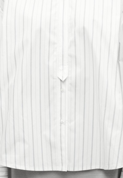 Λευκό πουκάμισο με λεπτές κάθετες γκρι ρίγες, εμπρόσθιο με κουμπιά και με μια μυτερή λεπτομέρεια πατιλέτας στο κέντρο.