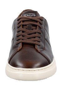 Hnědé kožené tenisky s kulatou špičkou, hnědými tkaničkami a bílou gumovou podrážkou. Obsahují malé logo na boku a švy.