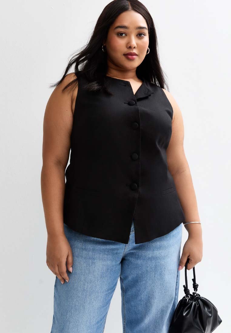 Chaleco negro sin mangas con cuello tipo solapa y cierre de botones en la parte delantera, combinado con jeans de mezclilla azul claro y un pequeño bolso negro.