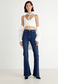 Λευκό κοντό τοπ, ανοιχτό μπλε ψηλόμεσες φαρδιές τζιν παντελόνες, υπερμεγέθεις λευκή πουκαμίσα ριγμένη, μαύρες μυτερές γόβες, κασκόλ με σχέδια δεμένο γύρω από τον λαιμό.