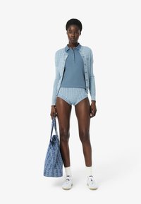 Valkoinen neulepusero, jossa on vaaleansininen sävy ja kaapeli kuvio, yhteensopiva yläosa ja korkeavyötäröiset housut. Kannan sinivalkoista kuviolaukku, yhdistettynä valkoisiin lenkkareihin.