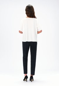 Top corto bianco a maniche corte, pantaloni neri a quadri a sigaretta e scarpe con tacco nere. Tessuto liscio e vestibilità comoda con dettagli di design minimi.