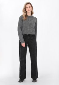 Pulover gri tricotat cu finisaj texturat, guler rotund și elemente decorative pe umeri. Pantaloni negri cu croi larg și cizme scurte.
