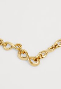 Gouden ketting met schakels die zijn samengevoegd in een gladde, gepolijste afwerking, met accenten in de vorm van een oneindigheidssymbool. Verstelbare sluiting.