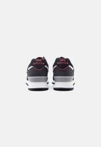 Ζευγάρι μαύρα και γκρι αθλητικά παπούτσια New Balance, εμφανιζόμενα από πίσω σε λευκό φόντο, με κόκκινο λογότυπο και λευκές μεσαίες σόλες.