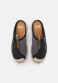 Chaussures noires à enfiler avec une tige en maille, semelle beige et languette en cuir brun. Équipées d'une semelle en liège et d'un logo sur le côté.
