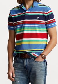 Kortärmad polotröja i blått med flerfärgade horisontella ränder. Tyget är strukturerad bomull. Har en klassisk krage och broderad logotyp.