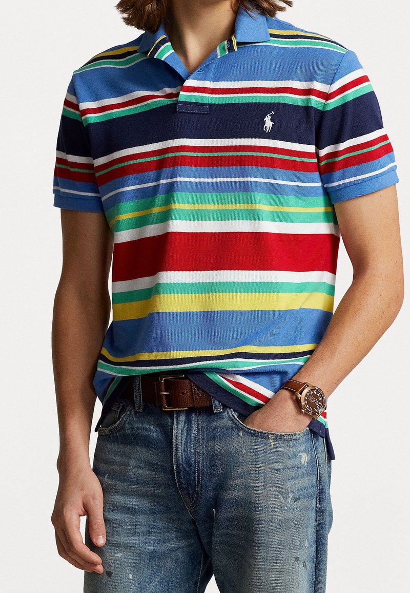 Kortärmad polotröja i blått med flerfärgade horisontella ränder. Tyget är strukturerad bomull. Har en klassisk krage och broderad logotyp.