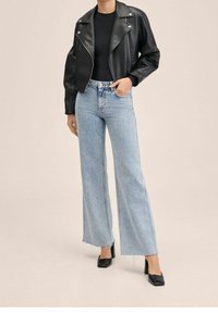 Sort læder cropped bikerjakke over en tætsiddende sort top. Lyseblå viddebenede jeans med frynset kant og strukturerede sorte hæle.