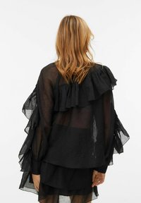 Černá průhledná blůza s volány na ramenou a rukávech, vrstvený design a dlouhé rukávy. Lehká, texturovaná látka.