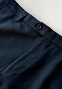 Marineblauwe, gestructureerde broek met voorzakken, een enkele knoopsluiting en een tailored ontwerp. Toont stiksel details en weefsel van de stof.