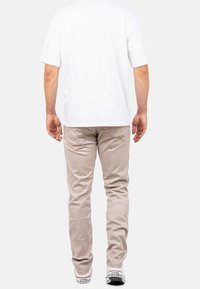 Pantalons en velours côtelé beige clair avec des côtes verticales, coupe slim, associés à un t-shirt blanc uni et des baskets blanches avec des accents noirs.