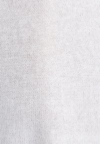 Tissu tricoté blanc avec un motif en boucles répétées montrant la texture et de petits interstices entre les points.