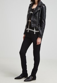 Svart läderbikersjacka med silverdetaljer, lager på en genomskinlig svart topp med vita geometriska mönster, tillsammans med smala svarta byxor och ankelstövlar.