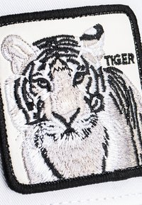 White patch featuring an embroidered tiger in beige and black threads, with detailed facial features. The patch has a black outline and the word "TIGER."