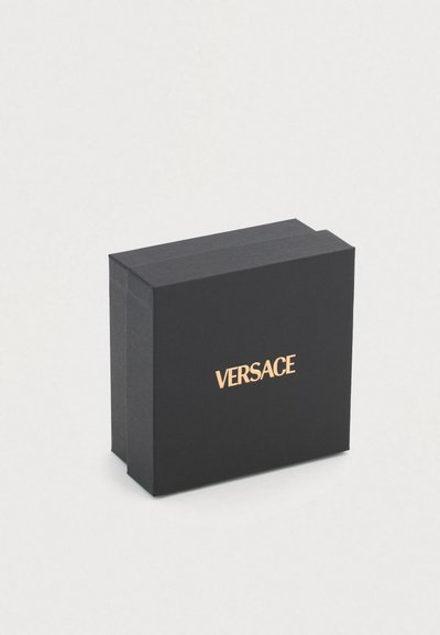 Juodas stačiakampis dėžutė su tekstūruota paviršiaus detalė, priekyje auksinis „VERSACE" logotipas. Tvarkingas dizainas, tinkantis prabangioms pakuotėms.