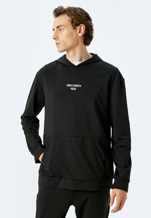 Sudadera con capucha negra de tejido suave, que cuenta con un bolsillo canguro en la parte frontal y texto blanco que dice "FUERZA ENFOQUE FOCO" en el pecho.