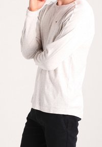 Harmaa pitkähihaisen paita, jossa on laikukuvio, pyöreä kaula-aukko ja ribattua hihansuut. Yhdistetty mustiin housuihin. Logo näkyvissä rinnassa.