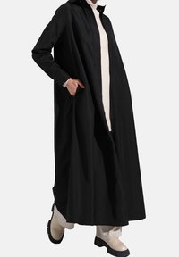 Long manteau noir à coupe droite, doté d'une fermeture éclair frontale, de poches latérales et d'un tissu lisse et léger.