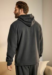 Tmavosivá, textúrovaná mikina s kapucňou, vyrobená z rebrovanej látky. Má dlhé rukávy a priame strih, s viditeľným prešívaním pozdĺž švov.