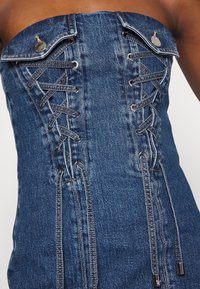 Haut corset en denim avec un design sans bretelles, des accents en métal et des détails à lacets sur le devant, de couleur bleu moyen.