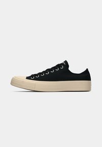 Black canvas sneakers with a cream rubber sole, rounded toe, six metal eyelets, and flat laces, featuring a low-profile design.
