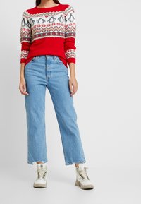 Röd stickad tröja med vita och grå mönster, i kombination med ljusblå högmidjade jeans och vita högklackade sneakers.