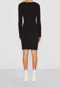 Black ribbed knit dress with a fitted silhouette, long sleeves, and a boat neckline. Worn with white ankle boots, highlighting leg shape.