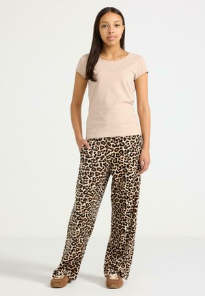 Béžové tričko s krátkým rukávem ve spojení s hnědými a černými širokými kalhotami s leopardím potiskem. Oblečení má boční kapsy a je vyrobeno z měkké látky.