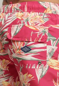 Bañadores florales con un vibrante fondo rosa, flores amarillas y hojas verdes, cinturilla elástica y un bolsillo trasero con logo.