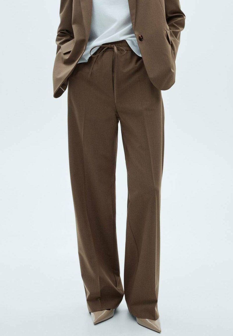 Pantalon marron à jambes larges avec taille à cordon, confectionné dans un tissu texturé, associé à un haut neutre et des chaussures à bouts pointus.