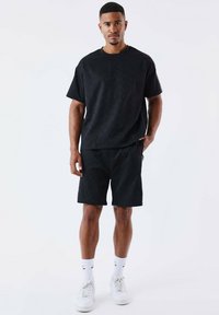 Black textured t-shirt and matching shorts, featuring a loose fit, with subtle patterns, and paired with white sneakers and socks.