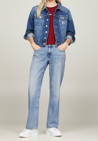 Chaqueta de mezclilla en azul oscuro, con bolsillos en el pecho y botones de metal, combinada con jeans azul claro y zapatillas blancas, con una camiseta burdeos debajo.