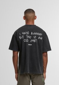 Muž s krátkým střihem stojí zády a nosí černé tričko s bílým nápisem "Nesnáším běhání, ale tohle je staré tričko."