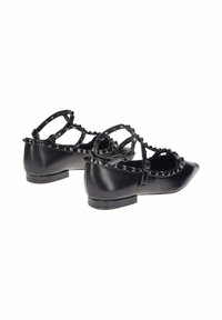 Ballerine in pelle nera con punte appuntite, borchie decorative lungo le cinghie e tacco basso. Le cinghie si incrociano sopra il collo del piede.