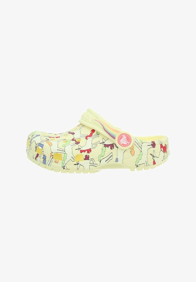 Jasnożółty chodak z wielobarwnymi wzorami jednorożców oraz paskiem z tyłu z motywem tęczy i okrągłym guzikiem z logo.