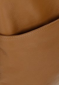 Tan leren handtas met een gestructureerde oppervlakte, met een afgeronde bovenrand en minimale stikdetails langs de naad.