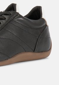 Μαύρο δερμάτινο αθλητικό παπούτσι με υφή, διαθέτει καφέ λαστιχένια σόλα, σχέδιο με κορδόνια και άσπρο τόνο στη φτέρνα.