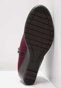 Bordeaux-farbene Ankle-Boots mit einer strukturierten schwarzen Gummisohle. Verfügbar mit einem seitlichen Reißverschluss und grauen Akzenten entlang der Ferse, die ein schlankes Design betonen.