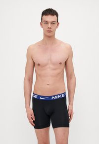 Fekete boxer alsónadrág kék Nike derékkal. Az anyag sima és rugalmas, térd fölötti hosszúsággal és testhez simuló dizájnnal rendelkezik.