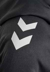 Dos formas de chevron blancas sobre una tela negra texturizada, probablemente parte de una prenda deportiva.