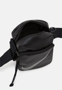 Černá nylonová crossbody taška s hlavním zipovým oddílem, přední kapsou a reflexním logem Nike. Obsahuje nastavitelný popruh a hladký povrch.