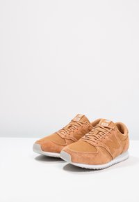 Beigesävyiset tennarit, joissa mokkanahka- ja verkkopäällinen teksturoidulla pinnalla, valkoinen kumipohja ja sivussa "N"-logo. Nauhallinen malli, hillityt yksityiskohdat.