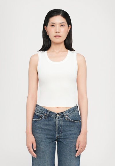 Top corto bianco a coste con scollatura rotonda. Abbinato a jeans in denim blu a vita alta, con una vestibilità rilassata e dettagli di cucitura classici.